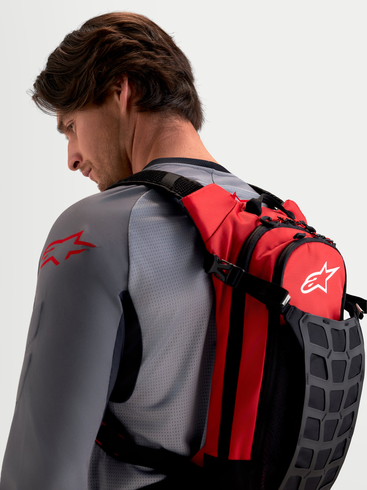 Alpinestars AT-9 rugzak, MX-rugzak gedragen door mannelijk model, rood en zwart textiel met gewatteerde schouderbanden en georganiseerde opbergruimte