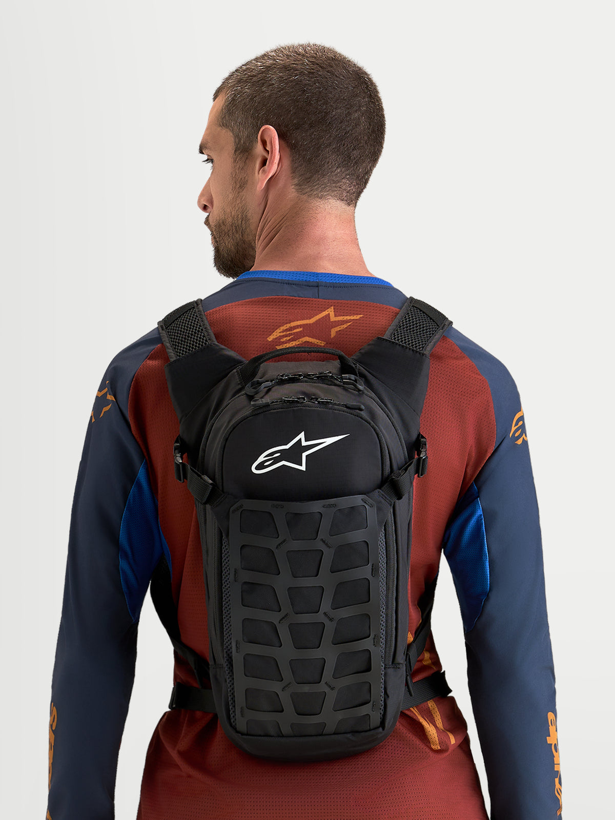 Alpinestars AT-9 rugzak, motocrossrugzak gedragen door een model, zwarte textielconstructie met wit Alpinestars-logo, compact design voor op het circuit en dagelijks gebruik
