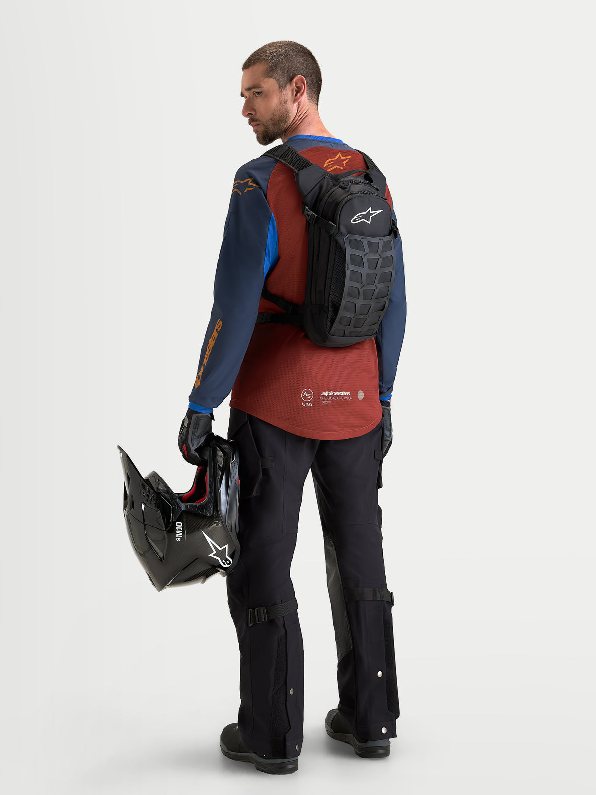 Alpinestars AT-9 rugzak, motocrossrugzak in zwart en donkergrijs, gedragen door een model van achteren met helm en bijpassende motoruitrusting