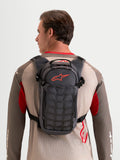 Alpinestars AT-9 rugzak, motocross rugzak gedragen door een model, walnoot- en donkergrijze textielconstructie met georganiseerde opbergvakken en een kenmerkend rood Astar-logo