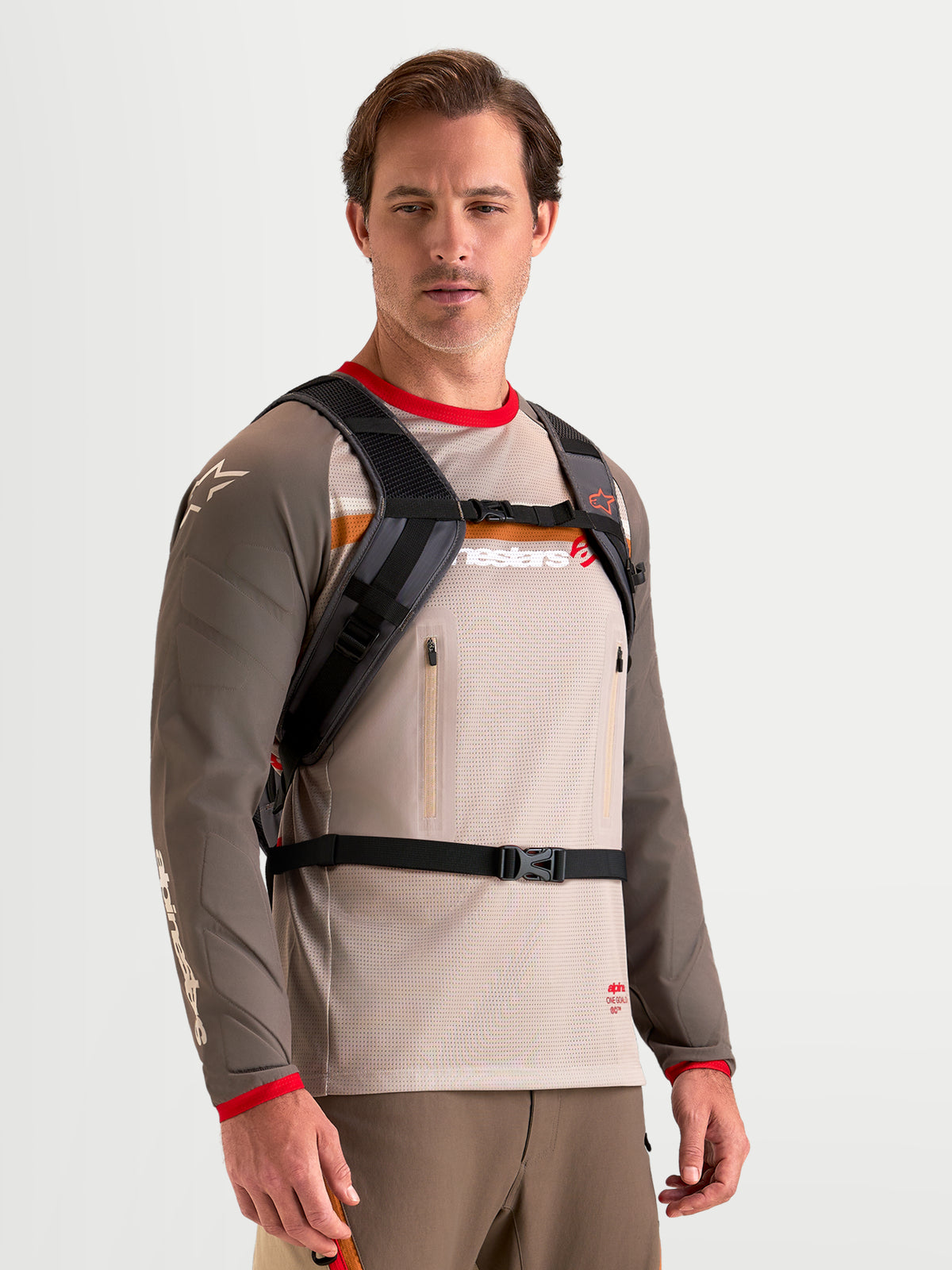 Alpinestars AT-9 rugzak, motorcrossrugzak in bruin en donkergrijs, gedragen door een mannelijk model met gewatteerd schouderharnas en gespsluitsysteem, lichte textielconstructie