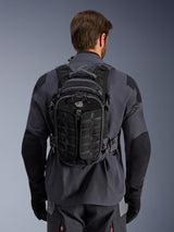 Alpinestars AT-15 Rugzak, adventure motorrugzak, Black Deep Gray, gedragen door een persoon over een grijs technisch motorjack, achteraanzicht met 'ALL TERRA' branding, ergonomisch ontwerp met versterkte panelen met textuur en stevige riemen.