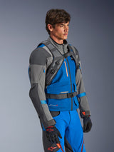 Alpinestars AT-15 Back Pack, Adventure motorrugzak, donkergrijs en diepgrijs, gedragen door een rijder over een blauw en grijs textiel motorjack, met de nadruk op het technische harnassysteem met borst- en taillegespen, ontworpen voor off-road stabiliteit