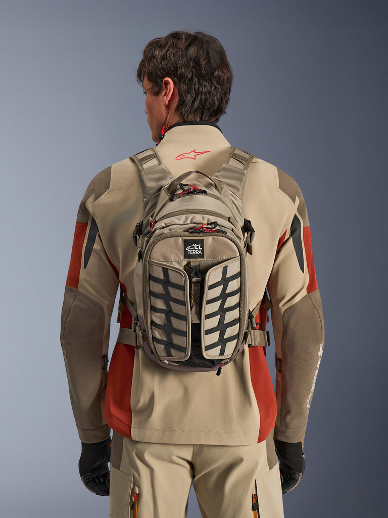 Alpinestars AT-15 rugzak, beige en zwart met rood, bandenprofiel patroon, motorfietsrugzak, draagbaar getoond, compacte opslag voor avontuurrijders
