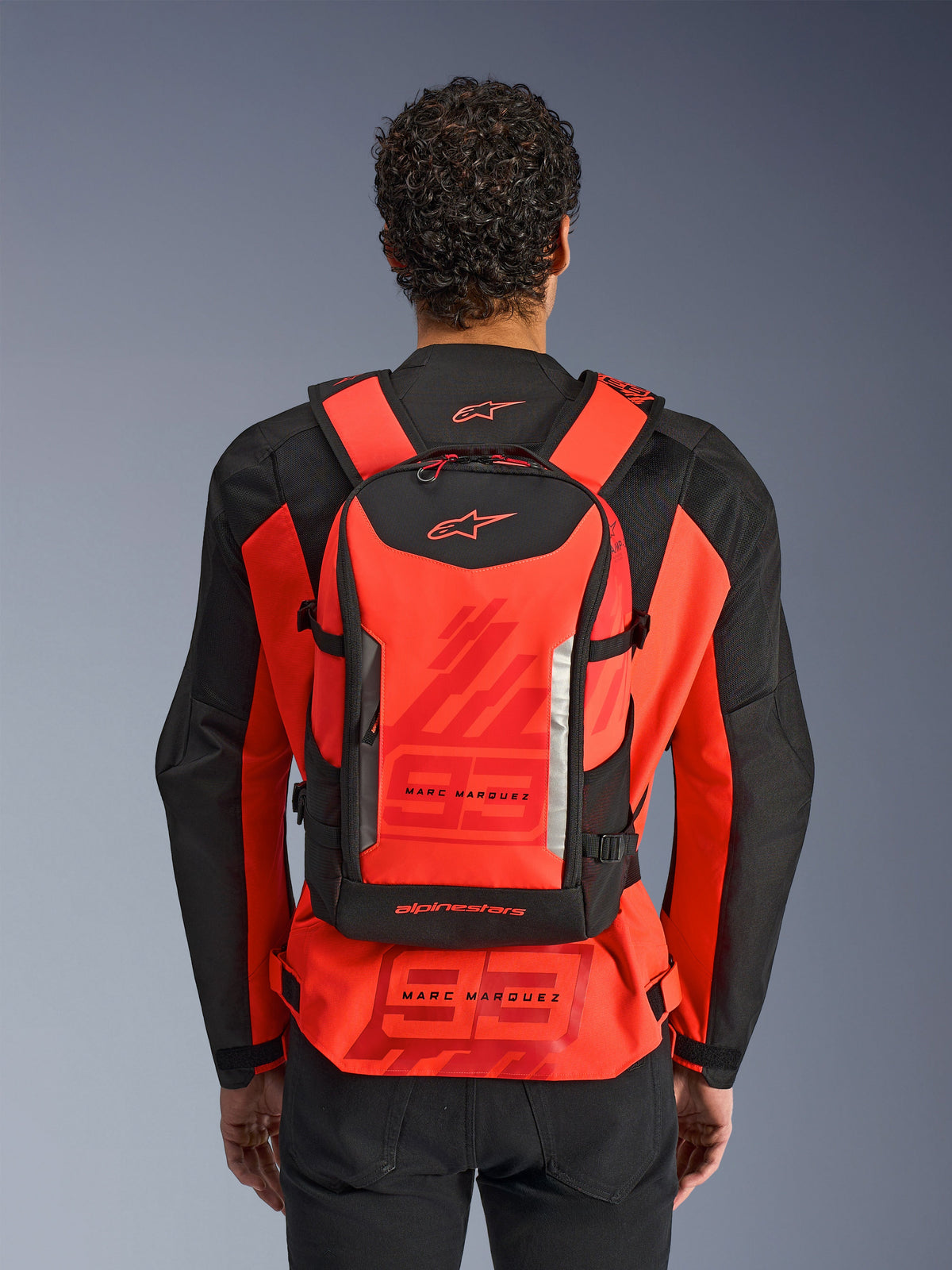 Alpinestars MM93 AMP3 rugzak, technische motorrugzak, fluo rood en zwart, van achteren gedragen door een motorrijder over een bijpassend rood en zwart MM93 racejack, voorzien van Marc Marquez-branding en Alpinestars-logo's