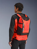 Alpinestars MM93 AMP3 rugzak, technische motorrugzak, fluorrood en zwart, gedragen door een model van achteren over een bijpassende rood-zwarte jas, voorzien van Marc Marquez '93' graphics, verstelbare banden en een strak sportief ontwerp.