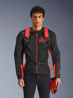 Alpinestars MM93 AMP3 rugzak, fluo rood en zwart, voorzien van verstelbare schouderbanden en borstriem met gesp, man draagt bijpassende MM93 motorjas en handschoenen, technische uitrusting uit de Marc Marquez-collectie