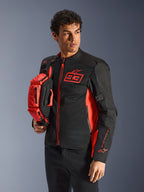 Alpinestars MM93 heuptas, fluorescerend rood en zwart, vastgehouden door een model in een bijpassende zwart-rode motorjas, voorzien van meerdere vakken met ritssluiting en Marc Marquez-branding, praktische uitrusting voor sportief rijden