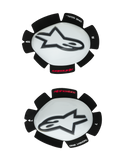 Alpinestars GP Tech kniesliders, motor kniebeschermers, wit en zwart, set van linker- en rechtersliders met witte plastic schalen en zwarte Astar-logo's, klittenband achterkant met 'ONE GOAL ONE VISION' tekst, hoogwaardige race-uitrusting