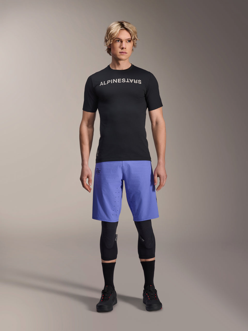 Alpinestars A-Aria Lite Short in Baja Blue, MTB-short voor heren, gedragen met een zwart shirt met korte mouwen en beschermende kniebeschermers, voorzien van laserperforaties voor ventilatie, mountainbike performance-uitrusting