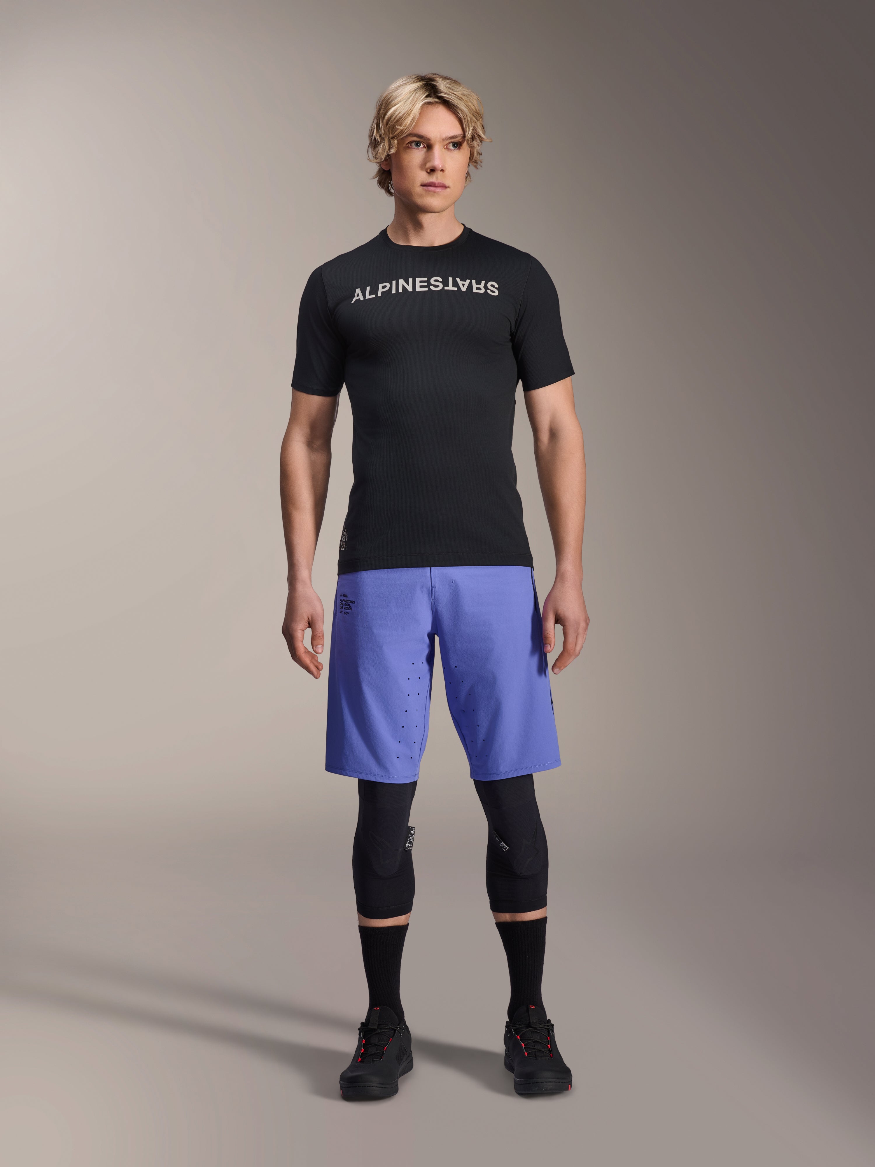 Alpinestars A-Aria Lite Short in Baja Blue, MTB-short voor heren, gedragen met een zwart shirt met korte mouwen en beschermende kniebeschermers, voorzien van laserperforaties voor ventilatie, mountainbike performance-uitrusting