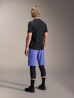 Mannelijk model van achteren in Alpinestars A-Aria Lite Shorts in Baja Blue, gecombineerd met een zwarte jersey met korte mouwen en zwarte kniebeschermers, professionele MTB-fietskleding voor trailrijden.