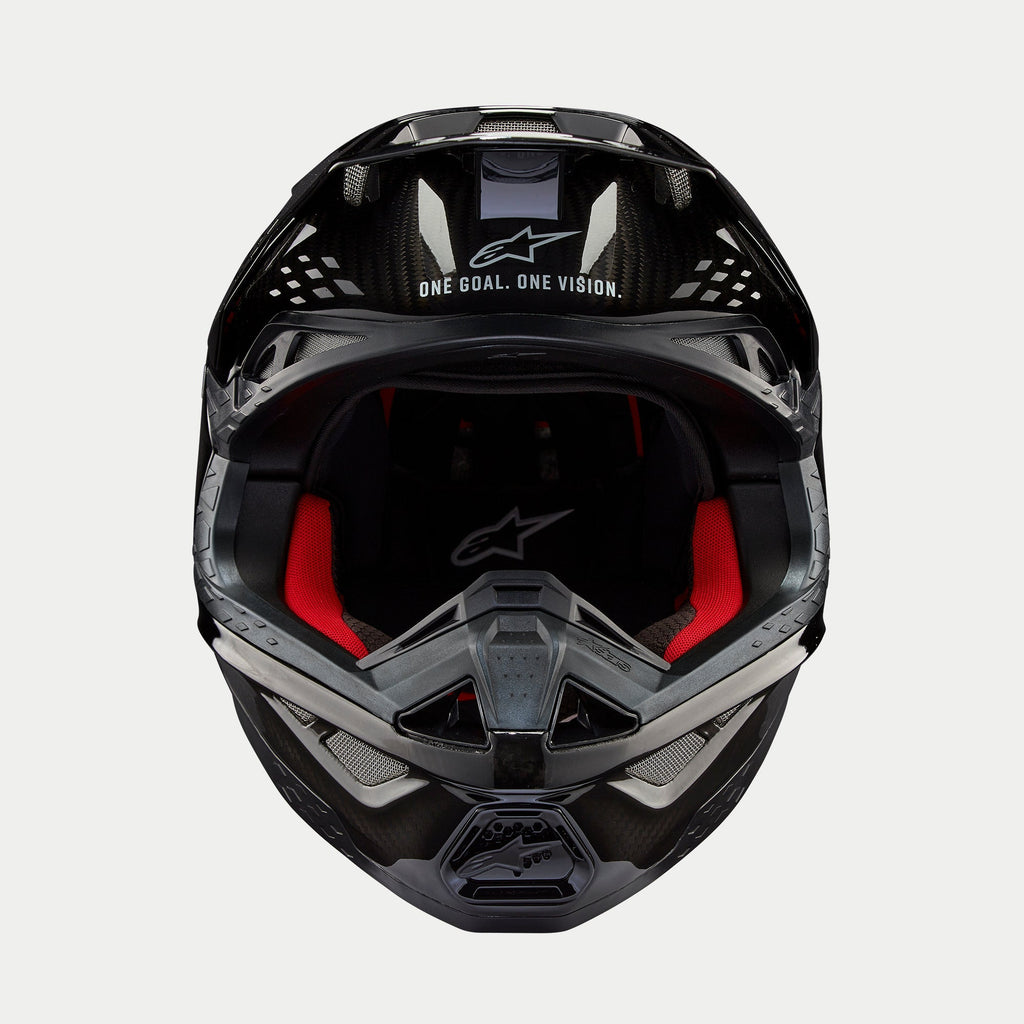 Alpinestars Supertech M10 Solid helm, motorcrosshelm, glanzend zwart carbon, vooraanzicht met rode binnenvoering, koolstofvezel helmschaal en 'ONE GOAL. ONE VISION.' slogan op het viziergedeelte