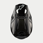 Alpinestars Supertech M10 Solid helm, motorcrosshelm, zwart glanzend carbon, bovenaanzicht met zichtbaar koolstofvezelweefsel, wit Astars-logo op de klep, slank aerodynamisch profiel met geïntegreerde ventilatieopeningen