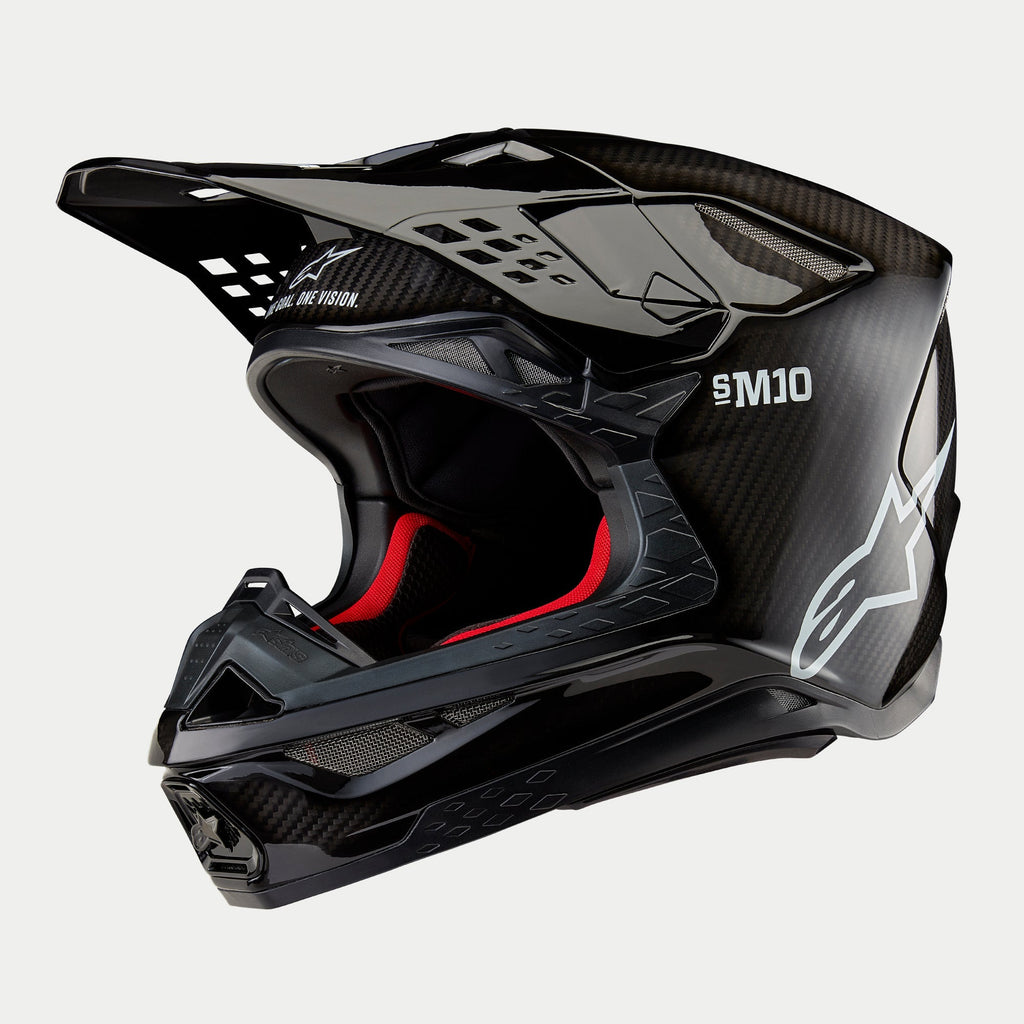 Alpinestars Supertech M10 Solid helm, motorcrosshelm, glanzend zwart carbon met zichtbaar vezelweefsel, voorzien van wit Alpinestars-logo en SM10-branding, rode binnenvoering, aerodynamisch ontwerp met meerdere ventilatieopeningen