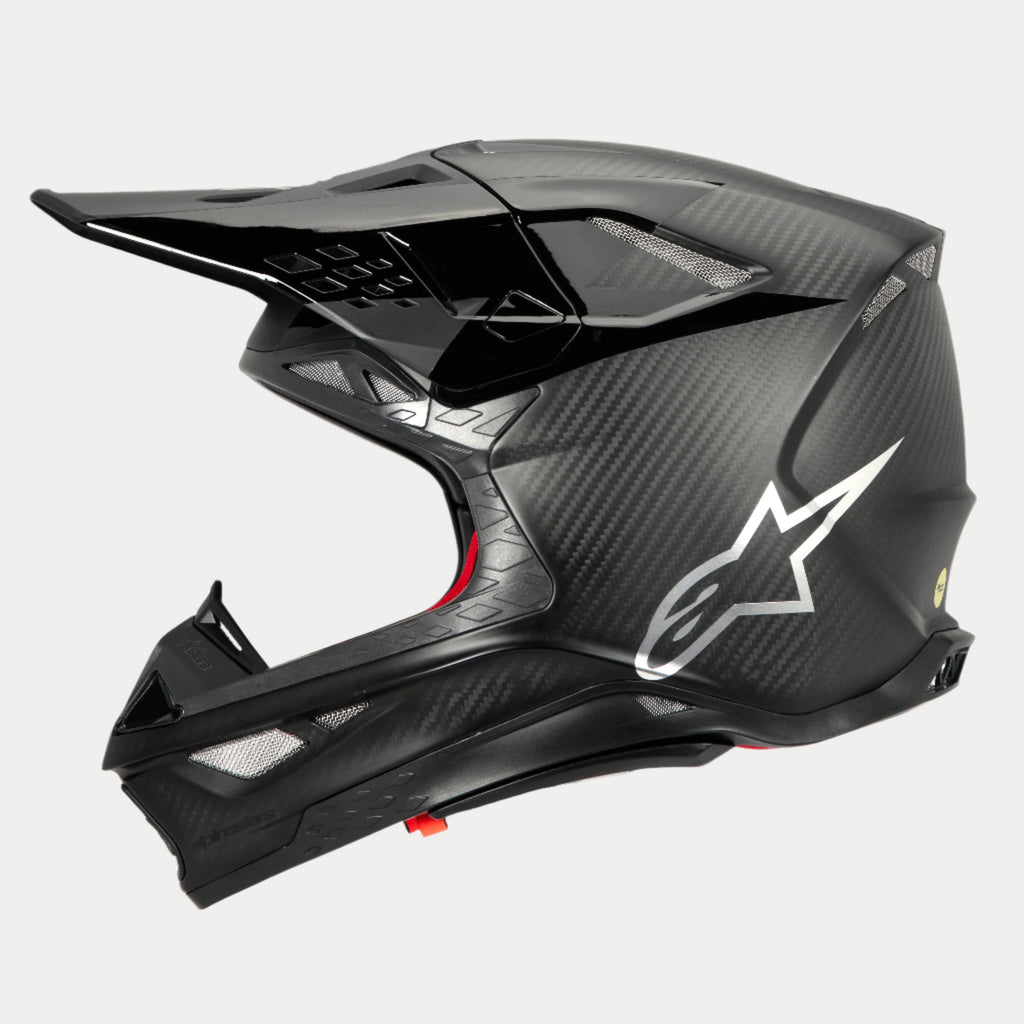 Alpinestars Supertech M10 Fame ECE 22.06 helm, zijaanzicht, mat en glanzend zwarte carbon-afwerking, voorzien van zichtbaar koolstofvezelweefsel, zilveren Astars-logo op de zijkant, aerodynamisch ontwerp met geïntegreerde ventilatieopeningen en zwart vizier