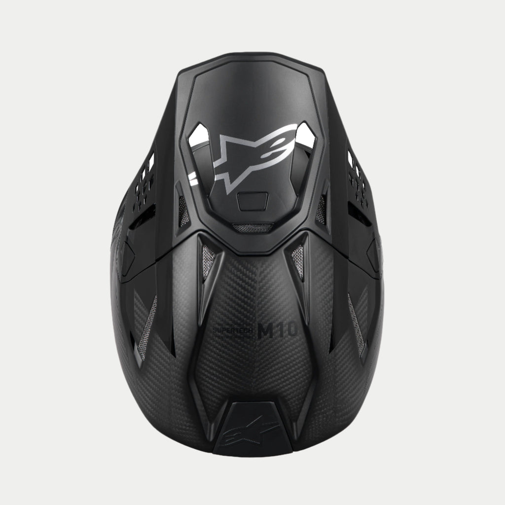Alpinestars Supertech M10 Fame ECE 22.06 helm, motorcrosshelm, zwart carbon mat en glanzend, bovenaanzicht dat de carbonvezelstructuur benadrukt, aerodynamisch vizier met zilveren Alpinestars-logo en meerdere ventilatiepoorten voor off-road racen.