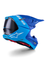 Alpinestars Supertech M10 Flood Helm, motocrosshelm, felblauw en marineblauw met zichtbaar zwart koolstofvezel, profiel achter-zijkant met ventilatieopeningen en wit logo, rode binnenvoering, geavanceerd aerodynamisch ontwerp voor off-road prestaties