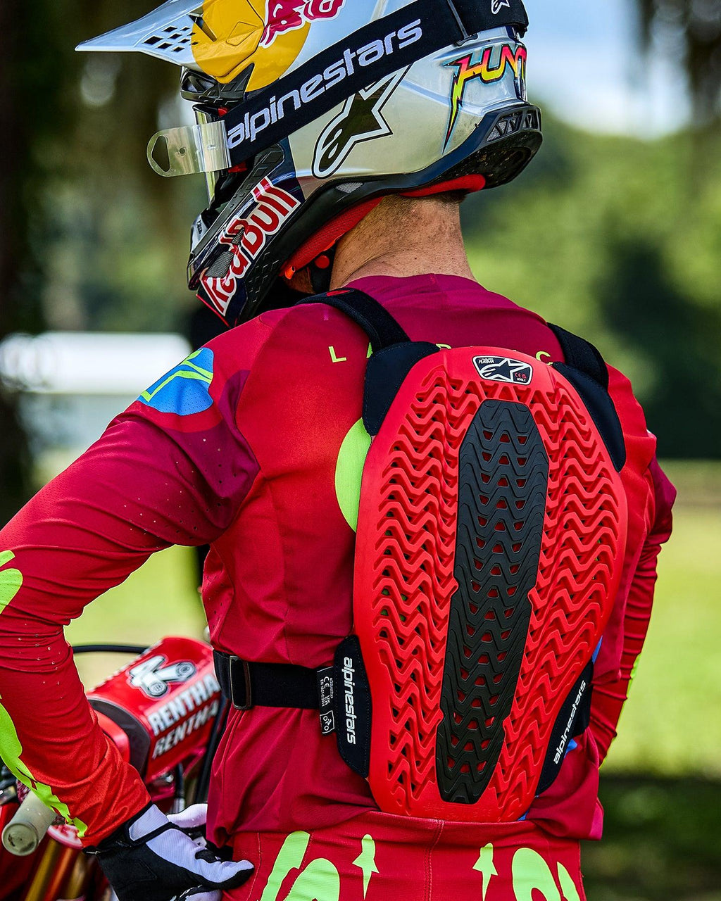 Alpinestars A-5 Plasma Borstbeschermer, rugbeschermer in rood en zwart met geventileerde honingraatstructuur, motocrossrijder van achteren gezien, rode jersey met lange mouwen en Red Bull helm