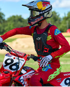 Motorcrossrijder met Alpinestars A-5 Plasma borstbeschermer in zwart en rood, gecombineerd met een rood en limegroen racejersey en broek, zittend op een rode Honda motorfiets, hoogwaardige off-road beschermende uitrusting