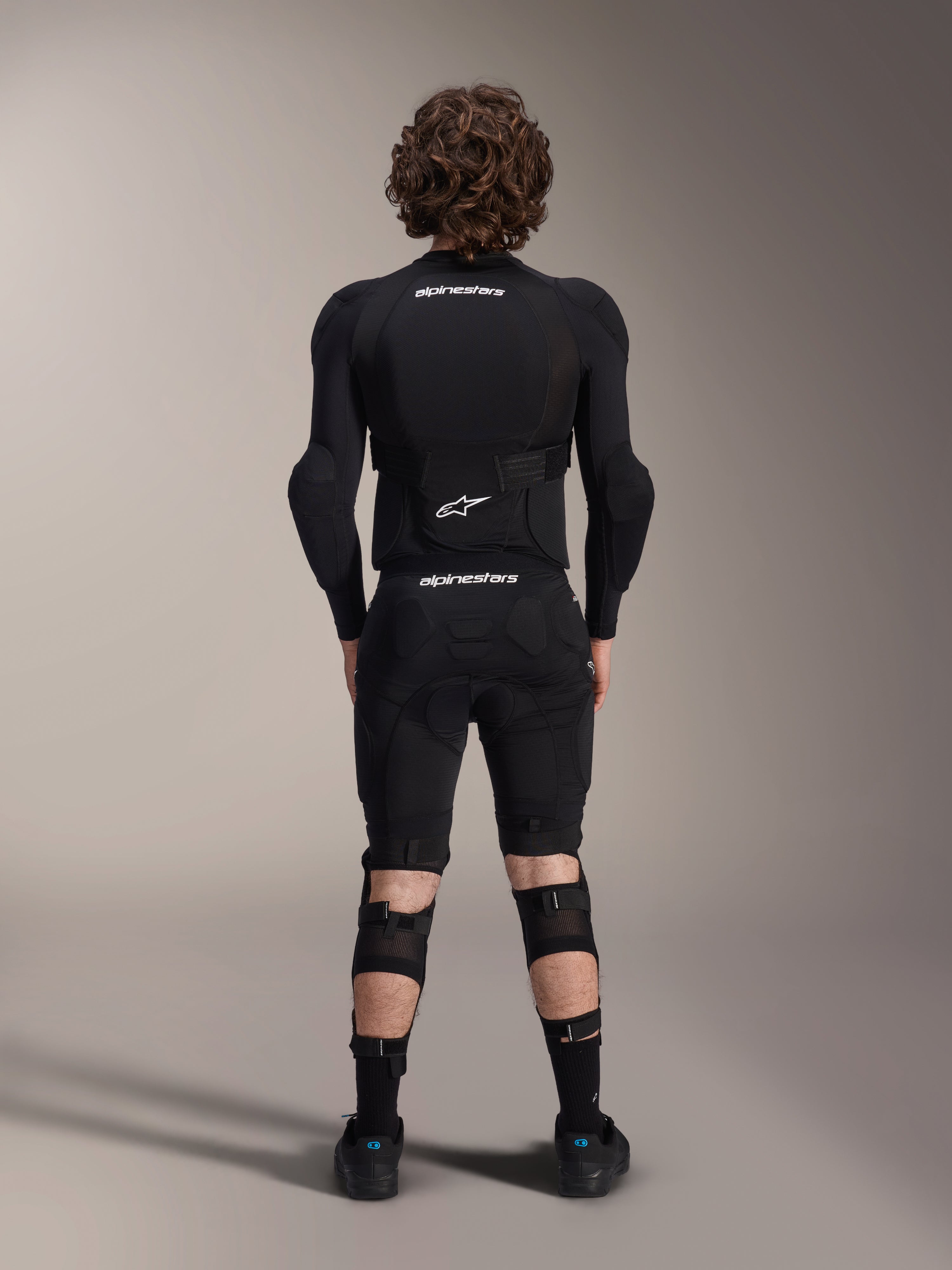 Alpinestars A-Impact Plasma Protection Jacket - Long Sleeve, back view, black with white Alpinestars logos, worn with protective shorts and knee guards for full-body mountain bike protection