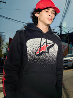 Alpinestars Obsessed Hoodie, zwarte fleece pullover, witte MX-verloop graphic op de borst met rood sterlogo, rode woordmerk-logo's op de mouwen, casual motorsport-geïnspireerde streetwear gedragen in een stedelijke omgeving.