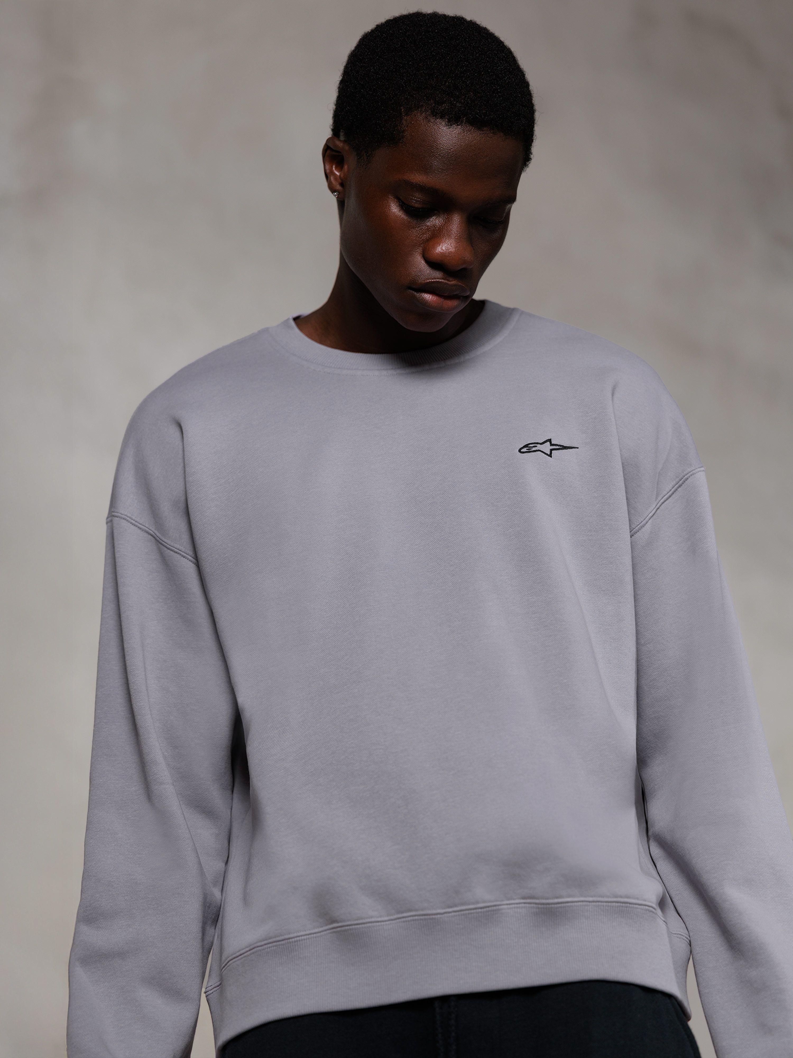 Alpinestars Essentials Ageless Crew, zilverkleurig premium sweatshirt met ronde hals, voorzien van een klein zwart Alpinestars-logo op de borst, gedragen door een model, casual lifestyle streetwear met een zachte fleece textuur.