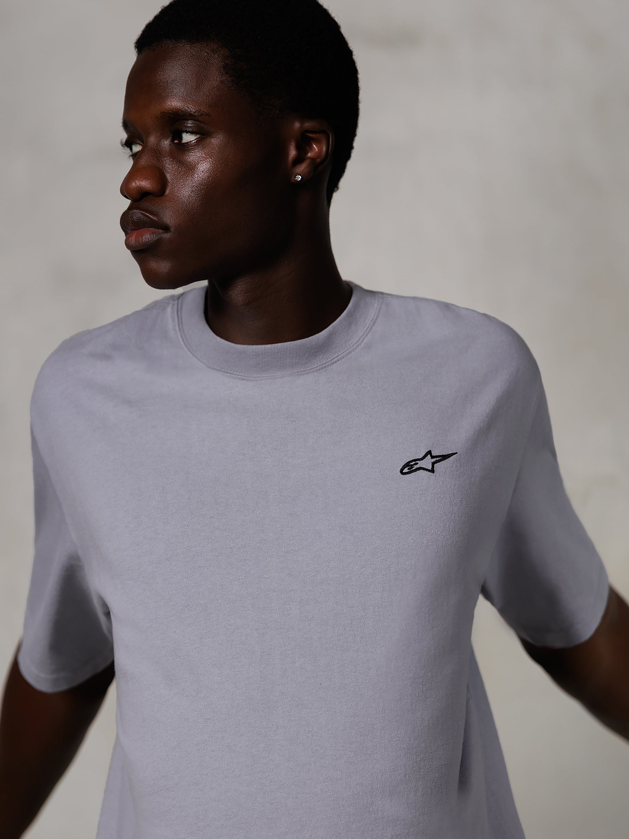 Model wearing Alpinestars Essentials Ageless SS Tee, Short Sleeve T-Shirt, Silver, featuring a small black logo on the chest, relaxed fit, clean and minimal streetwear design