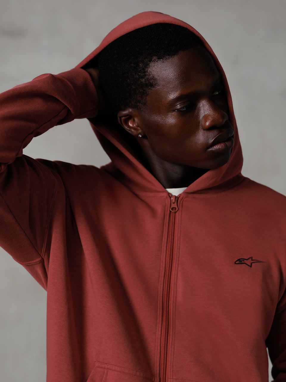 Alpinestars Essentials Ageless Zip Hoodie, steenrood, casual lifestyle streetwear, capuchon op met hand achter het hoofd, klein zwart Astars-logo op de borst, relaxed fit fleece hoodie