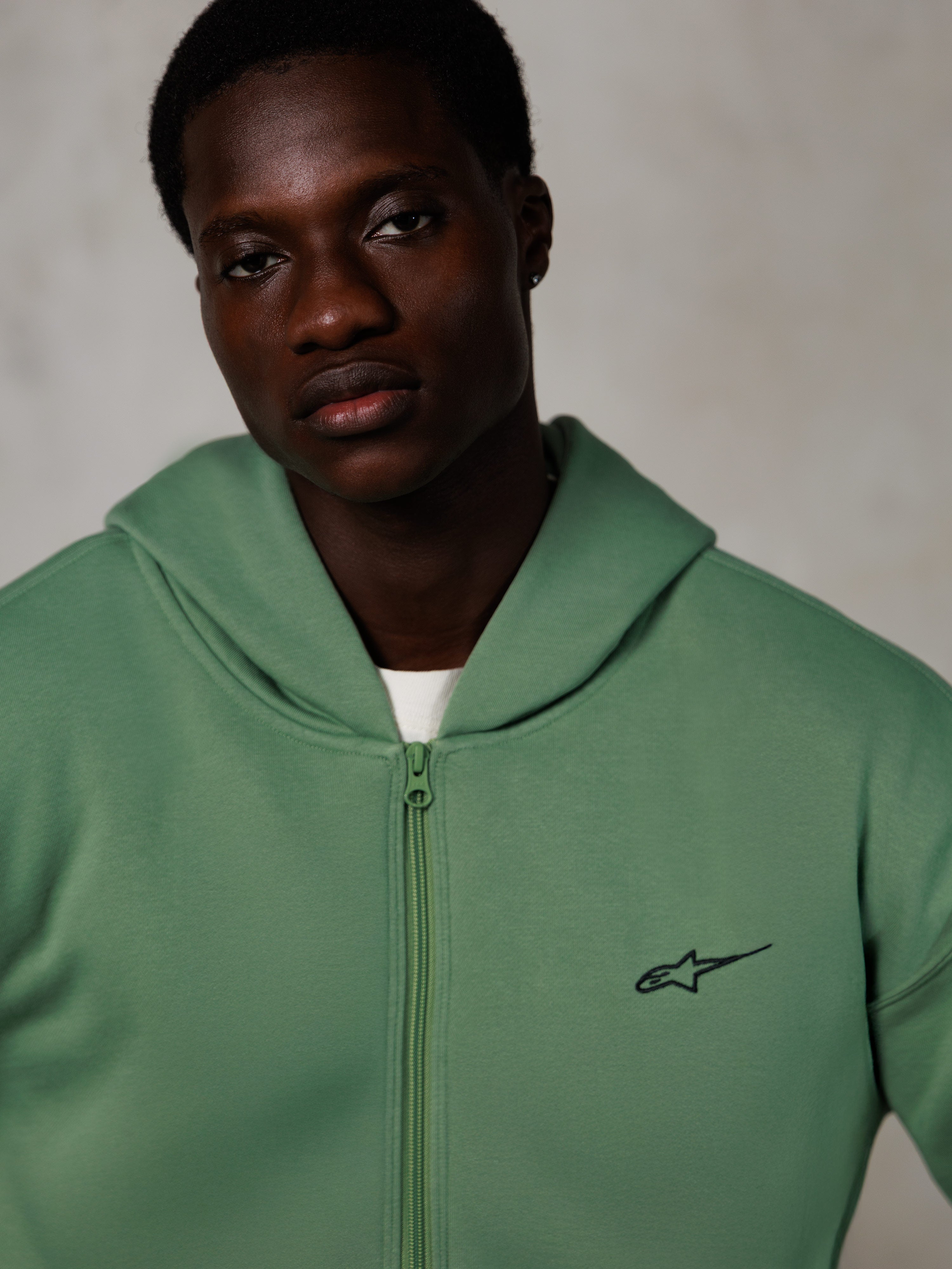 Alpinestars Essentials Ageless Zip Hoodie, lifestyle portret, cactusgroen met klein zwart logo, ritssluiting aan de voorzijde, zachte fleece textuur, casual op motorsport geïnspireerde streetwear