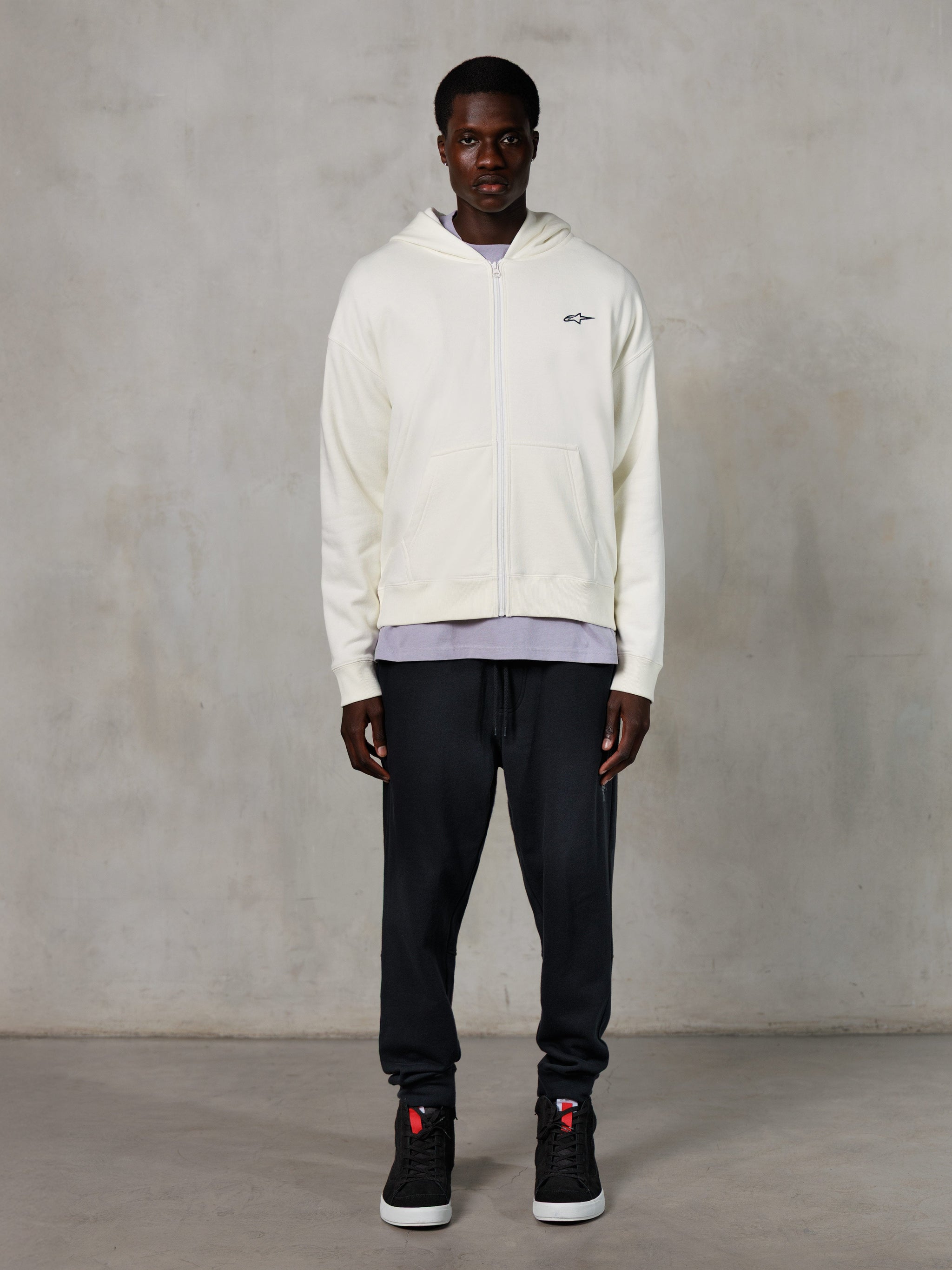 Alpinestars Essentials Ageless Zip Hoodie, casual streetwear, off-white met subtiel zwart borstlogo, volledige ritssluiting aan de voorzijde, ontwerp met capuchon, ontspannen pasvorm, gestyled met een zwarte joggingbroek en sneakers