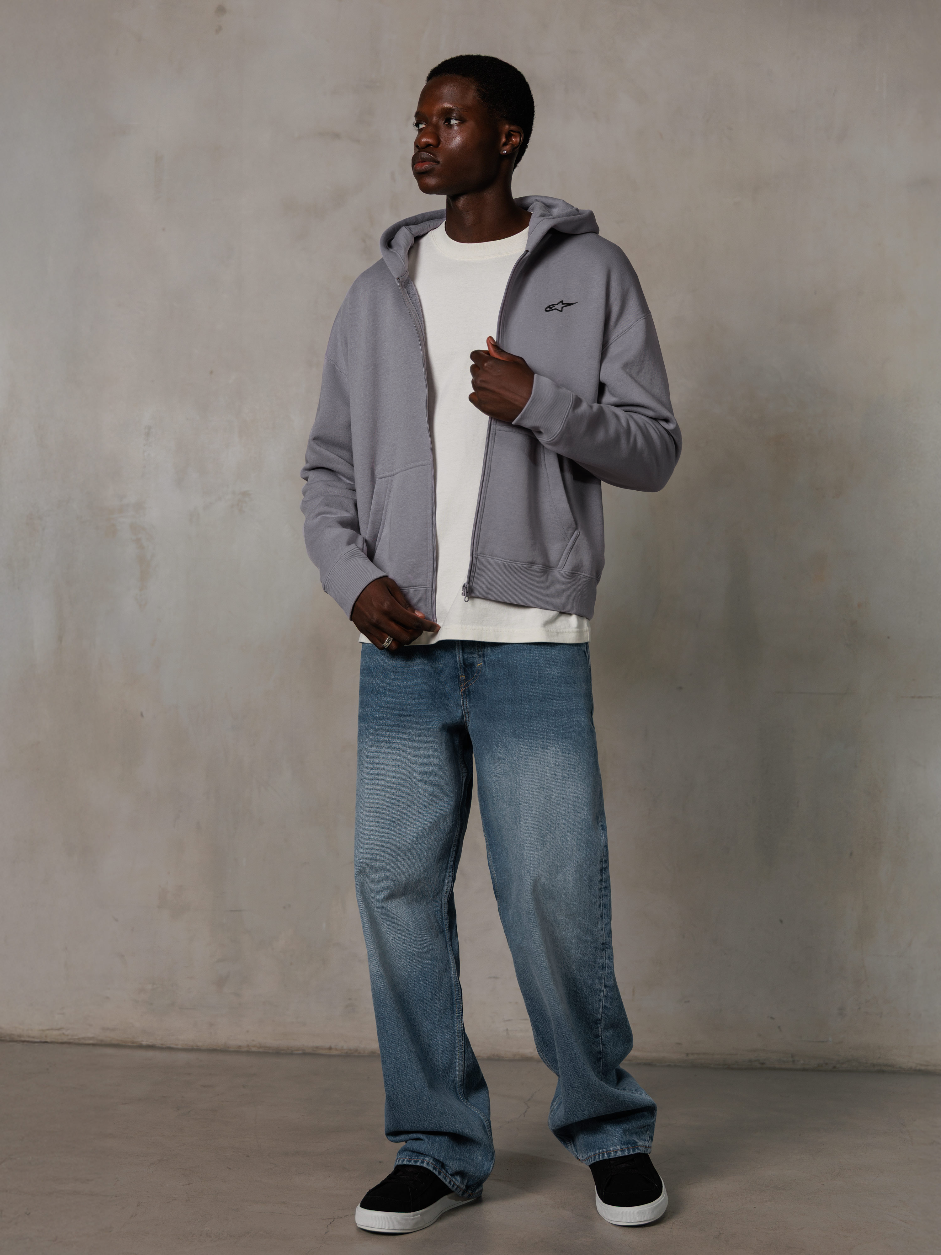 Alpinestars Essentials Ageless Zip Hoodie, Silver, casual streetwear, fleece hoodie met volledige ritssluiting en een klein zwart logo op de borst, gedragen door een model met een wit t-shirt en blauwe jeans, ontspannen lifestyle-pasvorm