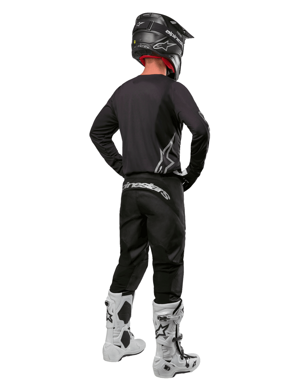 Alpinestars 2024 Fluid Graphite Gear Set, motorcrossrijder van achteren gezien, grafietgrijze jersey en broek met zilveren Alpinestars-logo's, zwarte helm en witte motorcrosslaarzen, atletische pasvorm voor off-road rijden