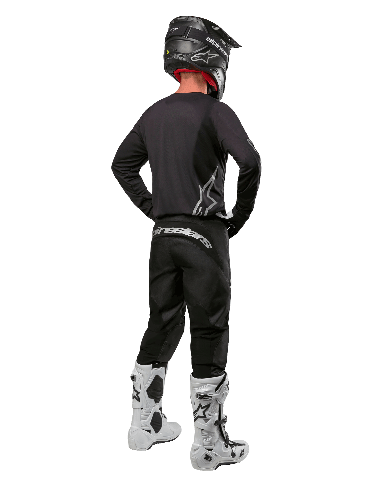 Alpinestars 2024 Fluid Graphite Gear Set, motorcrossrijder van achteren gezien, grafietgrijze jersey en broek met zilveren Alpinestars-logo's, zwarte helm en witte motorcrosslaarzen, atletische pasvorm voor off-road rijden