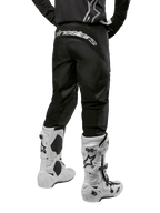 Alpinestars 2024 Fluid Graphite Gear Set, achteraanzicht van zwarte en grijze motorcrossbroek met wit Alpinestars logo op het zitvlak, gedragen met witte en zwarte motorcrosslaarzen, gespecialiseerde off-road race-uitrusting
