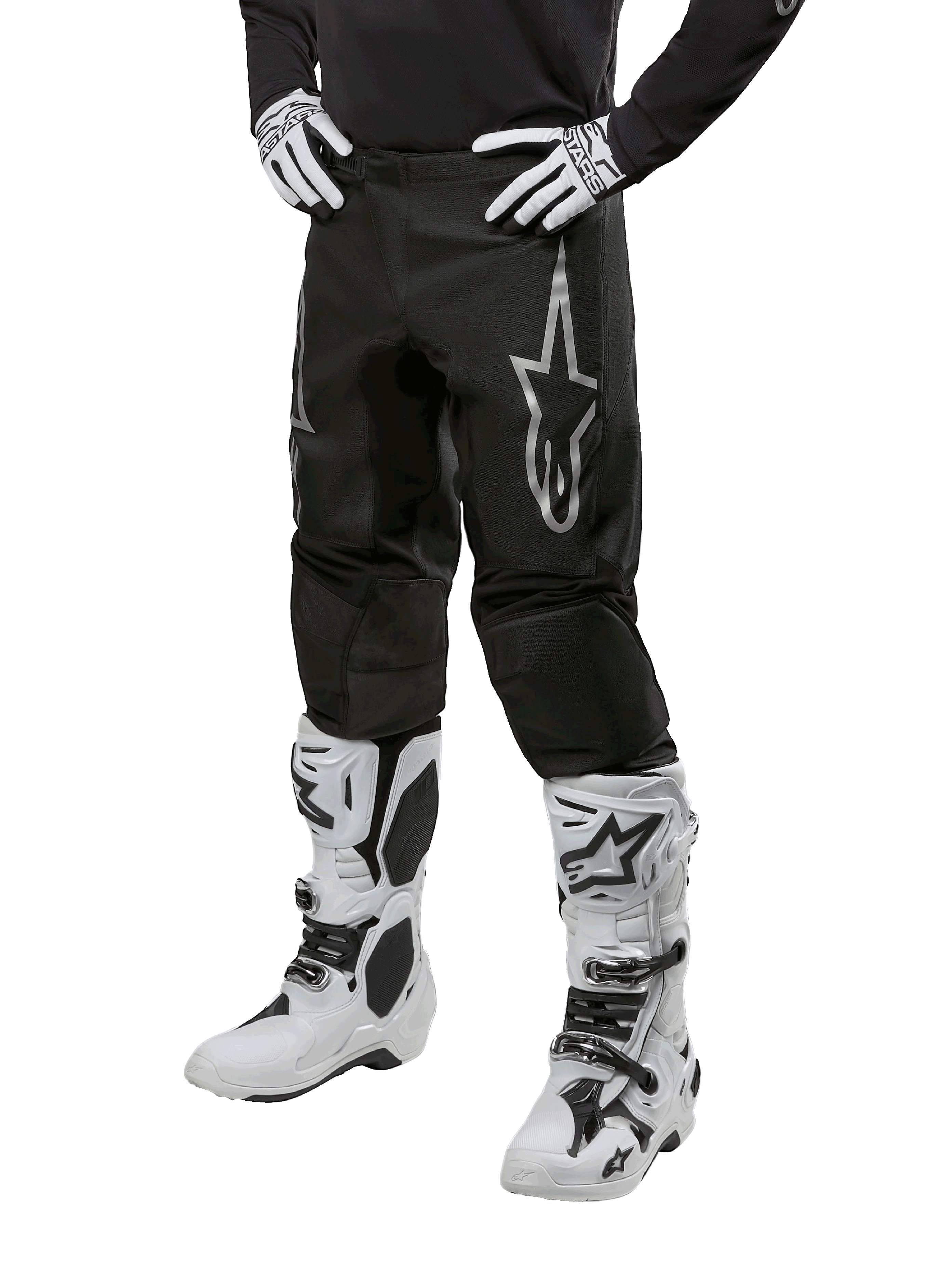 Alpinestars 2024 Fluid Graphite crossbroek, motorcross broek, grijs en zwart, gedragen met witte en zwarte motorcrosslaarzen en handschoenen, met een groot zilveren Alpinestars-logo op het bovenbeen, sportieve pasvorm voor off-road rijden