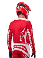 Alpinestars 2024 Fluid Lurv Jersey, motorcross shirt, Mars Red en wit, achteraanzicht met wit Alpinestars-logo op de rug en branding op de mouwen, gecombineerd met een bijpassende rode helm en zwarte handschoenen, professionele off-road race-uitrusting