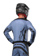 Alpinestars 2024 Fluid Lurv Jersey, motocross shirt, lichtblauw en zwart, achteraanzicht van rijder met groot sterlogo en branding op de mouwen, gedragen met een zwarte helm en bijpassende off-road broek, professionele racekleding