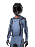 Motorcrosser in Alpinestars 2024 Fluid Lurv Jersey, lichtblauw en zwart, gecombineerd met zwarte helm en bril, voorzien van opvallende zwarte grafische accenten en Alpinestars-sterlogo, atletische performance-uitrusting voor off-road racen