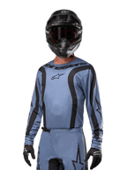 Motorcrosser in Alpinestars 2024 Fluid Lurv Jersey, lichtblauw en zwart, gecombineerd met zwarte helm en bril, voorzien van opvallende zwarte grafische accenten en Alpinestars-sterlogo, atletische performance-uitrusting voor off-road racen