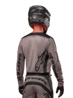 Motorcrossrijder van achteren gezien in de Alpinestars 2024 Fluid Lurv Jersey in Mud Black, met zwarte Alpinestars branding op de mouwen en rug, gecombineerd met een zwarte helm en bijpassende uitrusting voor off-road racen