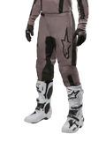 Alpinestars 2024 Fluid Lurv crossbroek, motorcrossbroek, Mud Black en zwart, voorzien van Alpinestars-logo, gedragen met zwarte handschoenen en witte motorcrosslaarzen, sportief ontwerp voor off-road racen