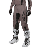 Alpinestars 2024 Fluid Lurv crossbroek, motorcrossbroek, Mud Black en zwart, voorzien van Alpinestars-logo, gedragen met zwarte handschoenen en witte motorcrosslaarzen, sportief ontwerp voor off-road racen