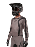 Alpinestars 2024 Fluid Lurv Jersey, motocross shirt, Mud Black en grijs, ontwerp met lange mouwen met gebogen zwarte strepen en logo's, gedragen met bijpassende broek en een zwarte motorcrosshelm, gecoördineerde off-road race-uitrusting