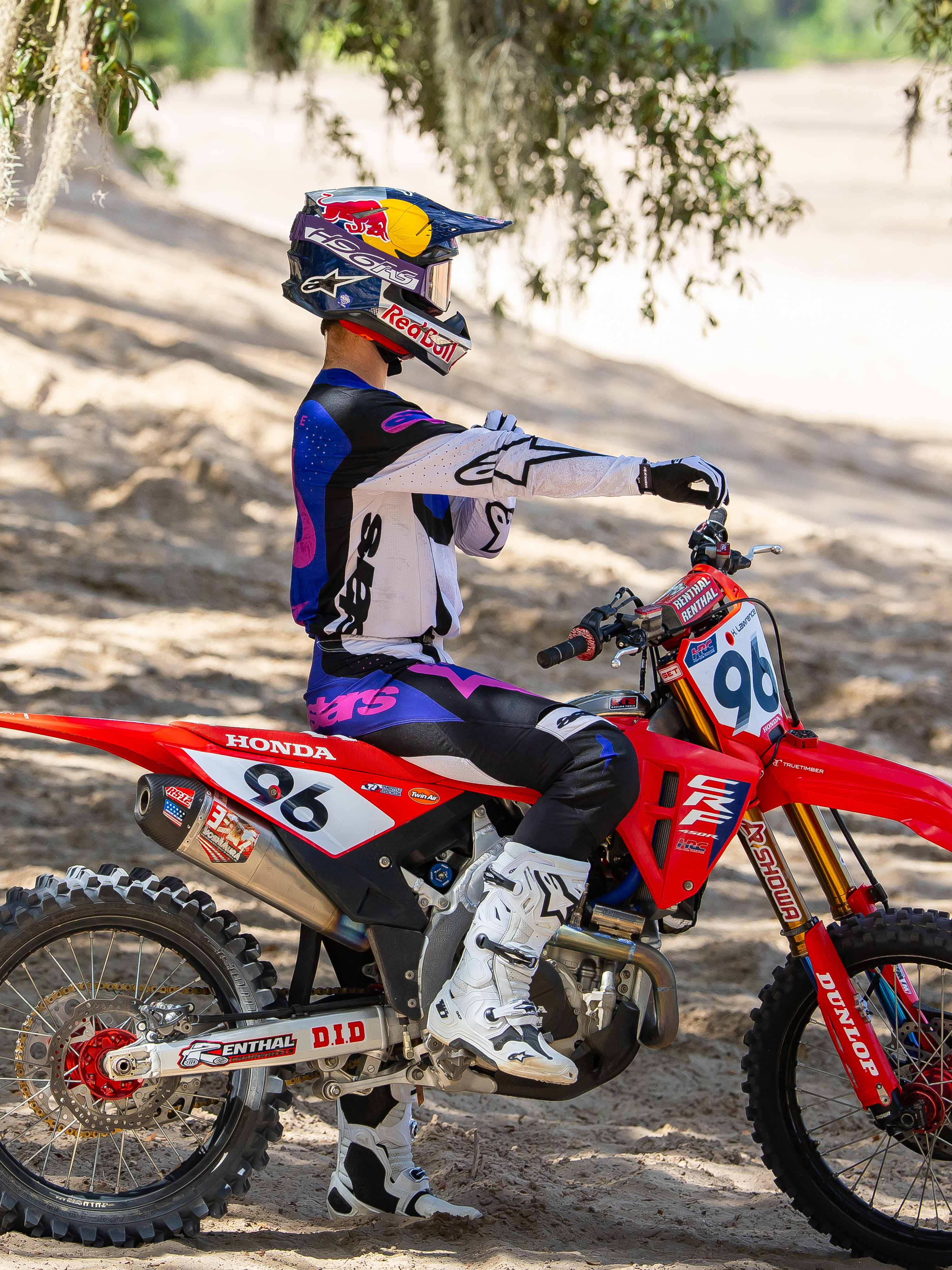 Motorcrosser met de Limited Edition HUNTA96 XXV Supertech Vision Goggles in Purple White Mirror Silver, bijpassende paars-witte motorcross jersey en witte laarzen, zittend op een rode Honda crossmotor met nummer 96, outdoor off-road setting op een zanderig circuit.