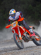 Motocross rider in action wearing Alpinestars Pro-Dura Jersey in Black, Bright Red, and White, riding an orange dirt bike on a dusty off-road trail, paired with black pants and red and white boots