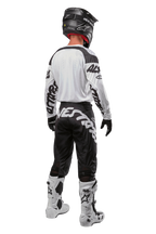 Alpinestars 2024 Racer Hana Pants, motorcross broek in zwart en wit, achteraanzicht, persoon draagt een volledige motorcross uitrusting met bijpassende jersey, helm en laarzen, sportief ontwerp voor terreinrijden