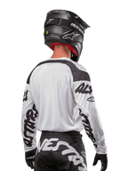 Alpinestars 2024 Racer Hana Jersey, wit en zwart, achteraanzicht met ergonomische pasvorm en opvallende branding op de mouwen, gecombineerd met een zwarte motorcrosshelm en bijpassende zwart-witte broek, hoogwaardige race-uitrusting voor off-road rijden