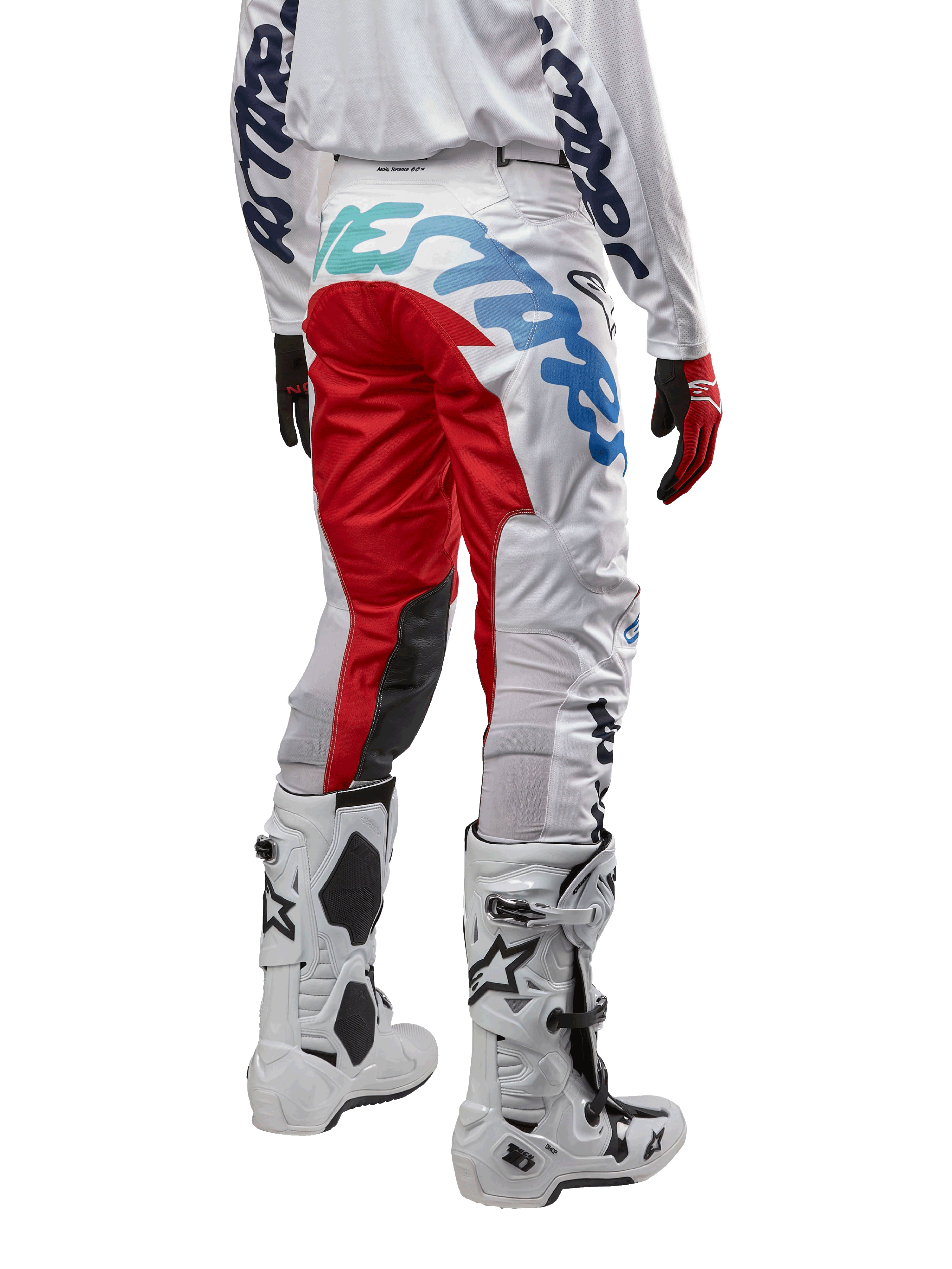 Alpinestars 2024 Racer Hana crossbroek, motorcrossbroek, wit multicolor met rode en blauwe accenten, achteraanzicht met grote branding op het zitvlak, gedragen met wit-zwarte motorcrosslaarzen, ontworpen voor off-road prestaties en duurzaamheid