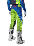 Alpinestars 2024 Racer Hoen crossbroek, motorcross broek, fluoriserend geel en donkerblauw (Blue Night Navy), achteraanzicht, voorzien van een rood Alpinestars-logo, gedragen met bijpassende jersey, witte handschoenen en witte motorcrosslaarzen, duurzaam textiel voor off-road racing